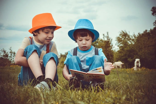 Deux garçons coiffés de chapeaux colorés assis dans l'herbe, l'un lisant un livre