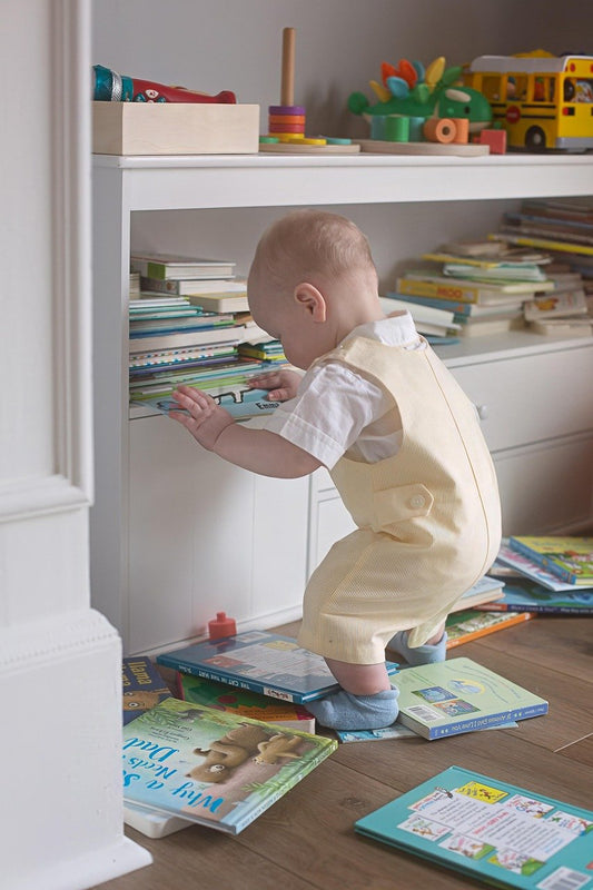Bébé debout retirant des livres d'une étagère basse entourée d'albums au sol