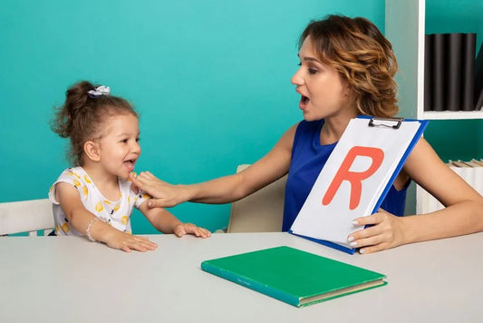 Orthophoniste montrant la lettre R sur un tableau à une fillette souriante assise à une table