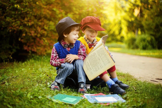 Deux enfants coiffés de chapeaux lisant un grand livre assis dans l'herbe
